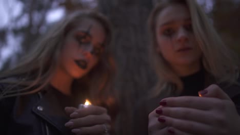 Dos-chicas-rubias-con-terrorífico-maquillaje-de-Halloween-sosteniendo-pequeñas-velas-en-las-manos-y-mirando-a-la-cámara