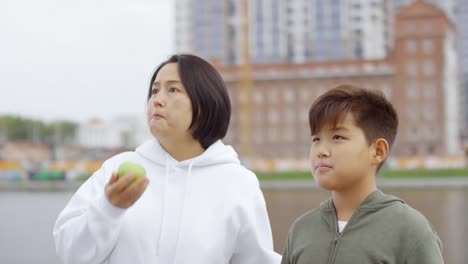 Asiatische-Mutter-und-Sohn-essen-Äpfel-am-Stadtufer