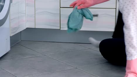 Woman-in-pink-rubber-gloves-washes-hard-kitchen-furniture-with-cloth.-sitting-on-the-floor.-Side-view.