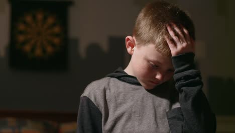 Sad-young-boy-standing-in-his-room-alone-and-looking-down-with-his-head-in-his-hands