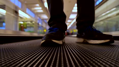 Vista-frontal-de-cerca-en-el-viajero-de-piernas-de-hombre-con-movimiento-plana-escalera-móvil-en-el-terminal-del-aeropuerto