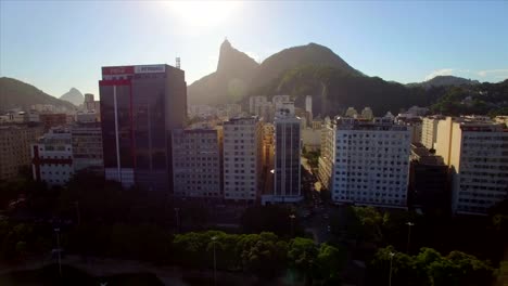 Rio-de-Janeiro-Aerial:-sideways-and-upwards-move-across-Botafogo-neighbourhood-revealing-Christ-the-Redeemer-behind-the-tall-buildings-at-sunset