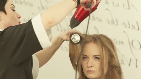 Mujer-rubia-en-cabello-largo-peinado-con-secador-y-cepillo-para-el-pelo-en-peluquería.-Cerca-de-haircutter-mujer-cabello-con-secadora-y-peine-después-de-lavado-y-corte