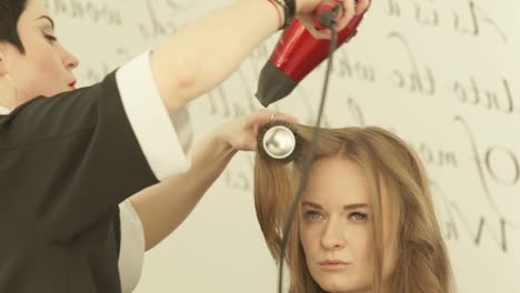 Blonde-Frau-bei-Frisuren-lange-Haare-mit-Trockner-und-Haarbürste-im-Friseursalon.-Nahaufnahme-Haircutter-Frau-Haare-mit-Trockner-trocknen-und-Kämmen-nach-Waschen-und-schneiden