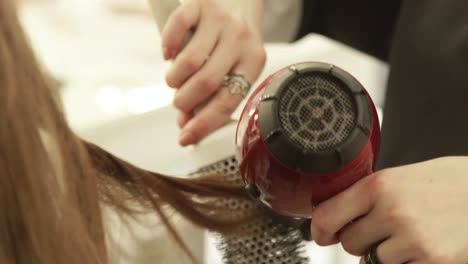 Haircutter-using-dryer-for-drying-female-hair-and-hairbrush-for-styling-after-hairdressing-in-beauty-studio.-Close-up-hairstylist-making-hairstyling-long-hair-in-hairdressing-salon