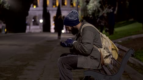 Mendigo-solitario-sentado-en-Banco-por-la-noche,-checar-su-limosna