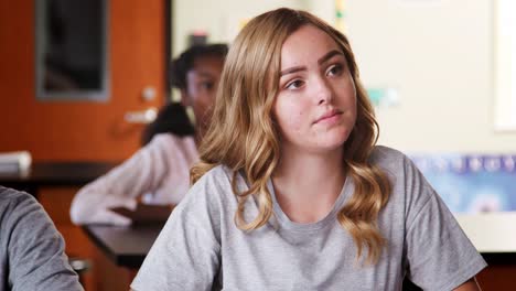 Group-Of-High-School-Pupils-Sitting-At-Desks-Listening-To-Teacher-In-Class