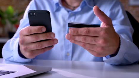 Close-footage-of-man-hands-paying-bills-with-credit-card,-purchasing-through-internet,-sitting-at-table