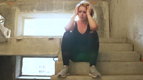 Young-unhappy-girl-is-sitting-at-the-stairs-in-an-abandoned-building