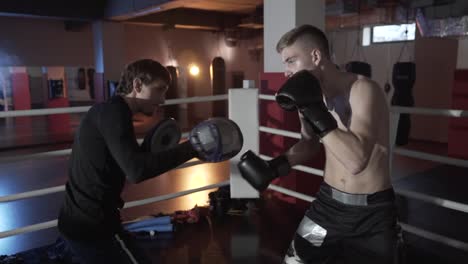 Der-junge-Boxer-spiegelt-die-Angriffe-des-Gegners.-der-Coach-beschäftigt-sich-mit-seiner-Ladung-in-den-Ring,-Angriffe-und-Attacken-ausweichen.-Close-up-Seitenansicht.-Das-Konzept-der-Boxen,-Ring,-Boxen-outfit