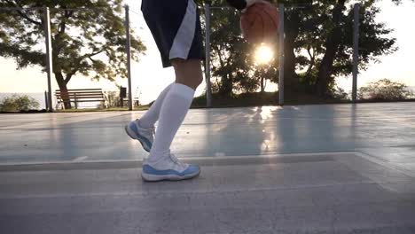 Close-up-footage-of-a-female-athlete-legs-in-white-golf-socks-and-sneakers.-Female-baasketball-player-bouncing-ball-from-hand-to-hand.-Sun-shines-on-the-background