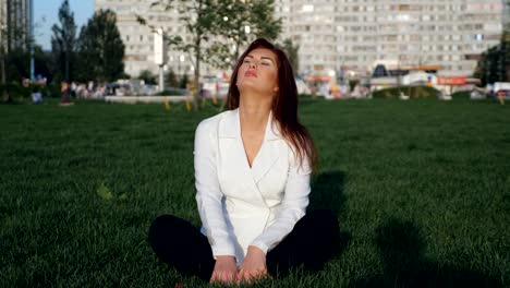 Young-businesswoman-in-white-suit-sitting-and-meditating-outdoor.