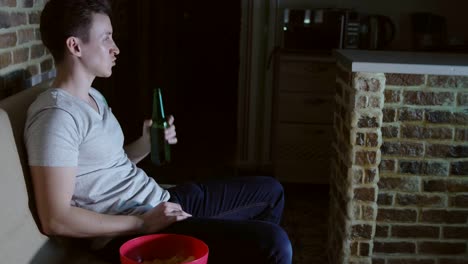 Man,-football-fan-is-drinking-beer-and-chips-in-front-of-TV