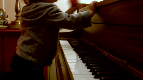 Caucasian-Toddler-Boy,-Sitting-at-a-Piano-with-Him-Mom,-Plays-on-the-Piano-with-a-decorated-Christmas-Tree-Behind-Them