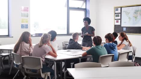 Mujer-alta-escuela-Tutor-permanente-por-mesa-con-estudiantes-enseñando-la-lección