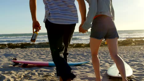 Hintere-Ansicht-paar-Hand-in-Hand-mit-Bierflasche-in-Richtung-Strand-4k