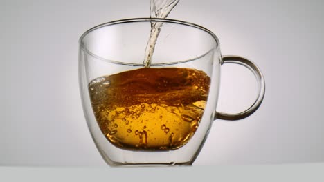 Pouring-tea-into-a-tea-glass-in-front-of-white-background-in-slowmotion