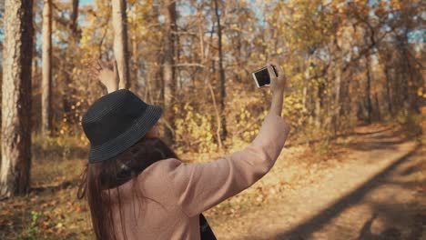 Young-blogger-girl-is-filming-herself-by-phone-on-walk-in-autumn-forest