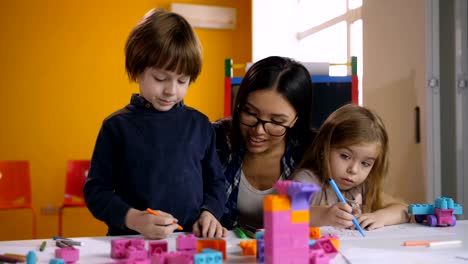 Teacher-helping-class-of-preschool-kids-to-draw