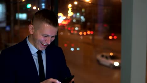 The-man-businessman-looks-at-the-smartphone-happy,-happy.-Outside-the-window,-against-the-night-city.