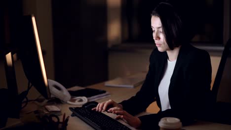 Mujer-de-negocios-en-traje-formal-trabaja-en-turno-de-noche-del-equipo-sentado-en-el-escritorio-escribiendo-y-mirando-la-pantalla.-Jóvenes-ocupados,-concepto-de-exceso-de-trabajo-y-carrera.