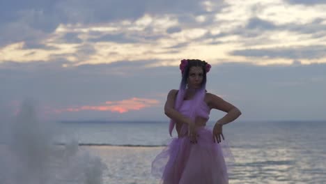 Cute-girl-with-sparkling-makeup-in-a-pink-dress-dancing-on-the-bank-of-the-river.-The-dance-of-a-sensual-woman-with-a-wonderful-hairstyle-with-flowers.-Slow-motion.