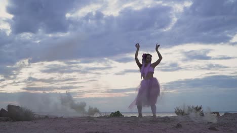 Hermosa-chica-con-maquillaje-brillante-en-vestido-rosa-bailando-en-la-niebla-de-bombas-de-humo-en-la-orilla-del-río.-El-baile-de-una-mujer-sensual-con-un-peinado-de-flor.-Cámara-lenta.