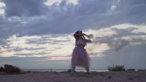 Joven-tierna-con-el-maquillaje-de-brillo-en-un-vestido-rosado-bailando-con-bombas-de-humo-al-aire-libre.-El-baile-de-una-chica-sensual-con-un-peinado-maravilloso-con-flores.-Cámara-lenta.