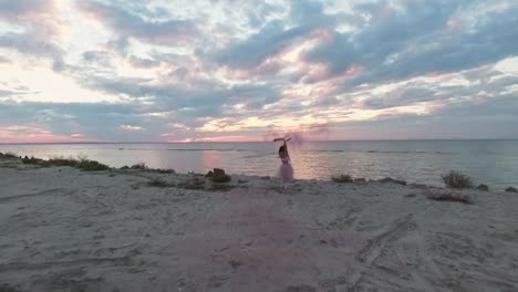 Auf-Sicht-auf-sinnliche-junge-Frau-mit-funkelnden-Make-up-in-einem-rosa-Kleid-tanzen-mit-Rauchbomben-am-Ufer-des-Flusses.-Der-Tanz-ein-ziemlich-süßes-Mädchen.-Slow-Motion.-Aufnahmen-aus-der-Drohne.