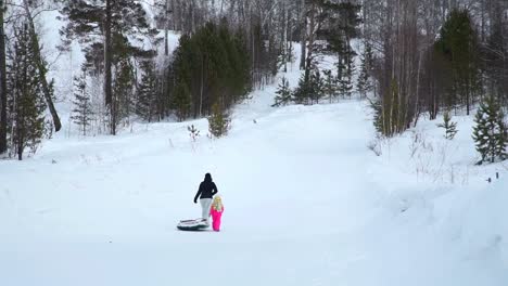 Mom-and-Daughter-Climbing-a-Hill-with-Snow-Tube