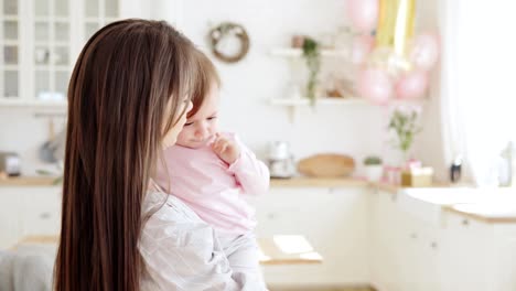 Loving-young-mother-holding-crying-baby-daughter-in-her-arms,-soothing-and-talking-to-her