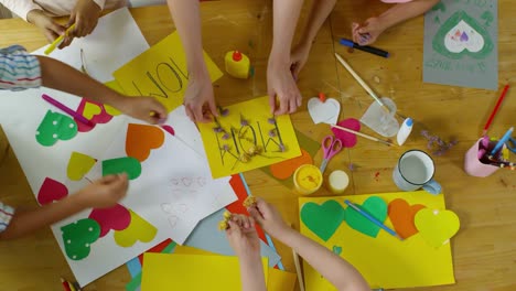 Vista-superior-de-las-manos-de-los-niños-poner-flores-en-la-tarjeta-de-felicitación-para-mamá