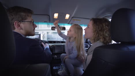 buying-of-family-transport,-father-with-mother-with-sweet-little-child-girl-giving-thumbs-up-while-examine-new-vehicle-in-salon-in-auto-dealership