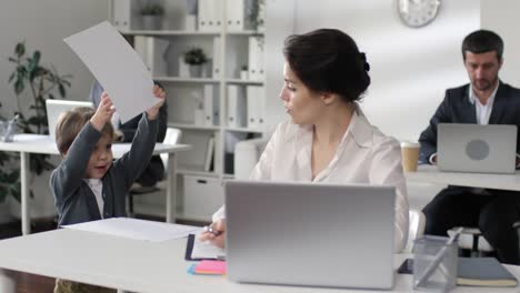 Mamá-de-negocios-trabajando-en-la-oficina-y-jugando-con-el-hijo-pequeño