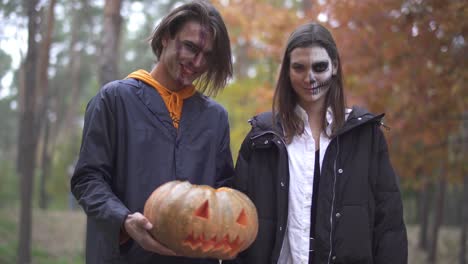 Alto-hombre-guapo-sosteniendo-calabaza-de-Halloween-con-una-luz-dentro,-chica-bonita-de-pie-cerca,-ambos-sonriendo-y-haciendo-caras-malvadas.