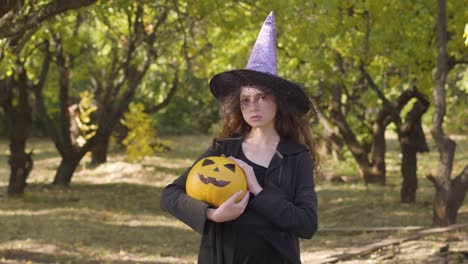 Bonita-pelirroja-caucásica-vestida-con-traje-de-bruja-de-Halloween-de-pie-en-el-parque-de-otoño.