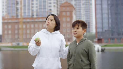 Madre-e-hijo-asiáticos-comiendo-manzanas-y-hablando-en-Urban-Riverside