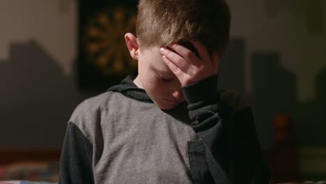 Sad-young-boy-standing-in-his-room-and-looking-down-with-his-head-in-his-hands