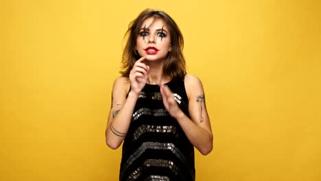 Crazy-nervous-woman-with-painted-eyes-and-lips-showing-silence-gesture-and-looking-side-to-side-isolated-over-yellow