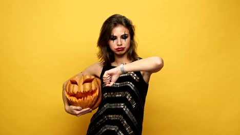 Young-nervous-displeased-lady-with-scary-make-up-playing-with-pumpkin-and-waiting-isolated-over-yellow