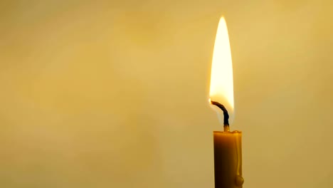 Close-up-of-a-wax-candle-burns-on-a-yellow-background.-4K.