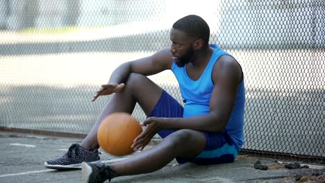 Nervous-man-in-sportswear-sitting-alone-near-stadium-and-holding-ball,-loser