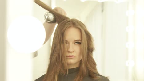 Junge-Frau-beim-Trocknen-lange-Haare-mit-Trockner-und-Haarbürste-Frontspiegel-im-Friseursalon.-Hautnah-Friseur-Haar-der-Frau-mit-Trockner-trocknen-und-kämmen-Sie-im-Beauty-salon