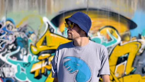 Portrait-of-adult-man-is-standing-with-a-graffiti-painting-in-the-background-and-glancing-around