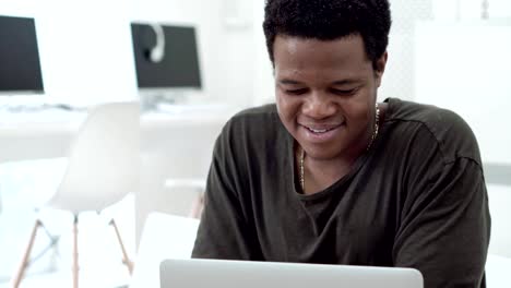 Medium-shot-of-Black-young-man-smiling-while-texting-in-social-net-in-Internet-cafe