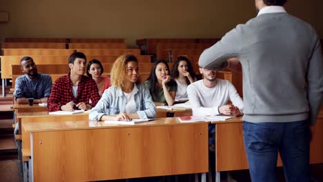 Multiracial-students-are-raising-hands-and-answering-teacher's-questions,-guy-in-glasses-gives-correct-answer-and-is-boasting-about-it.-Classmates-and-college-concept.