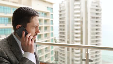 Businessman-angrily-talking-on-phone,-standing-on-balcony.-Big-city-background