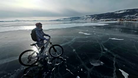 Frau-läuft-neben-dem-Fahrrad-auf-dem-Eis.-Das-Mädchen-trägt-einen-silbrig-down-Jacke,-Rucksack-und-Helm.-Eis-des-zugefrorenen-Baikalsees.-Die-Reifen-am-Fahrrad-sind-mit-speziellen-Spitzen-bedeckt.