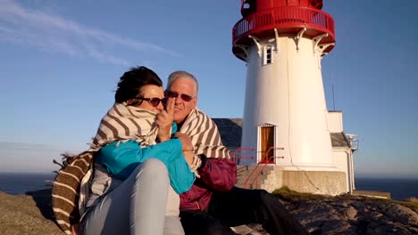 Ein-älteres-paar-bewundert-den-Sonnenuntergang-am-Meer-mit-einem-alten-Leuchtturm.