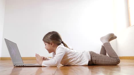 A-little-girl-lying-on-the-floor-uses-the-computer-and-looks-into-the-camera-and-smiles.